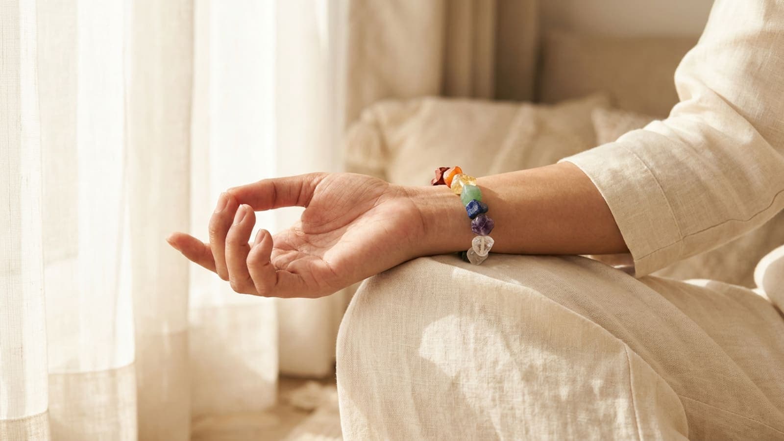 Woman's left wrist wearing a 7 chakra bracelet with seven natural stones during morning meditation by a window