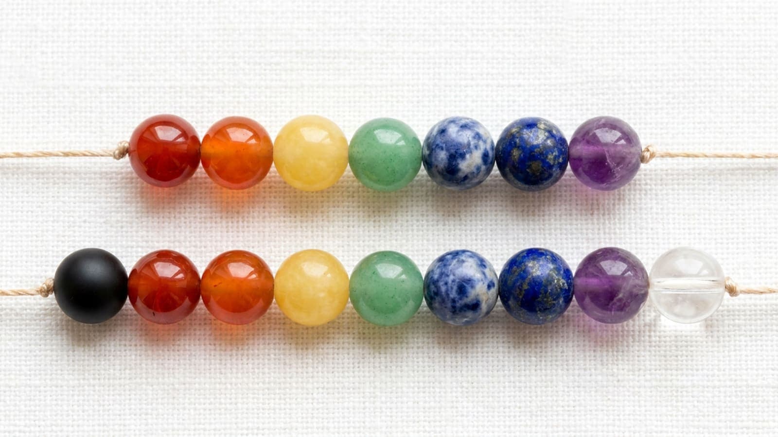 Nine-bead chakra bracelet laid beside a seven-bead chakra bracelet on white cloth for comparison