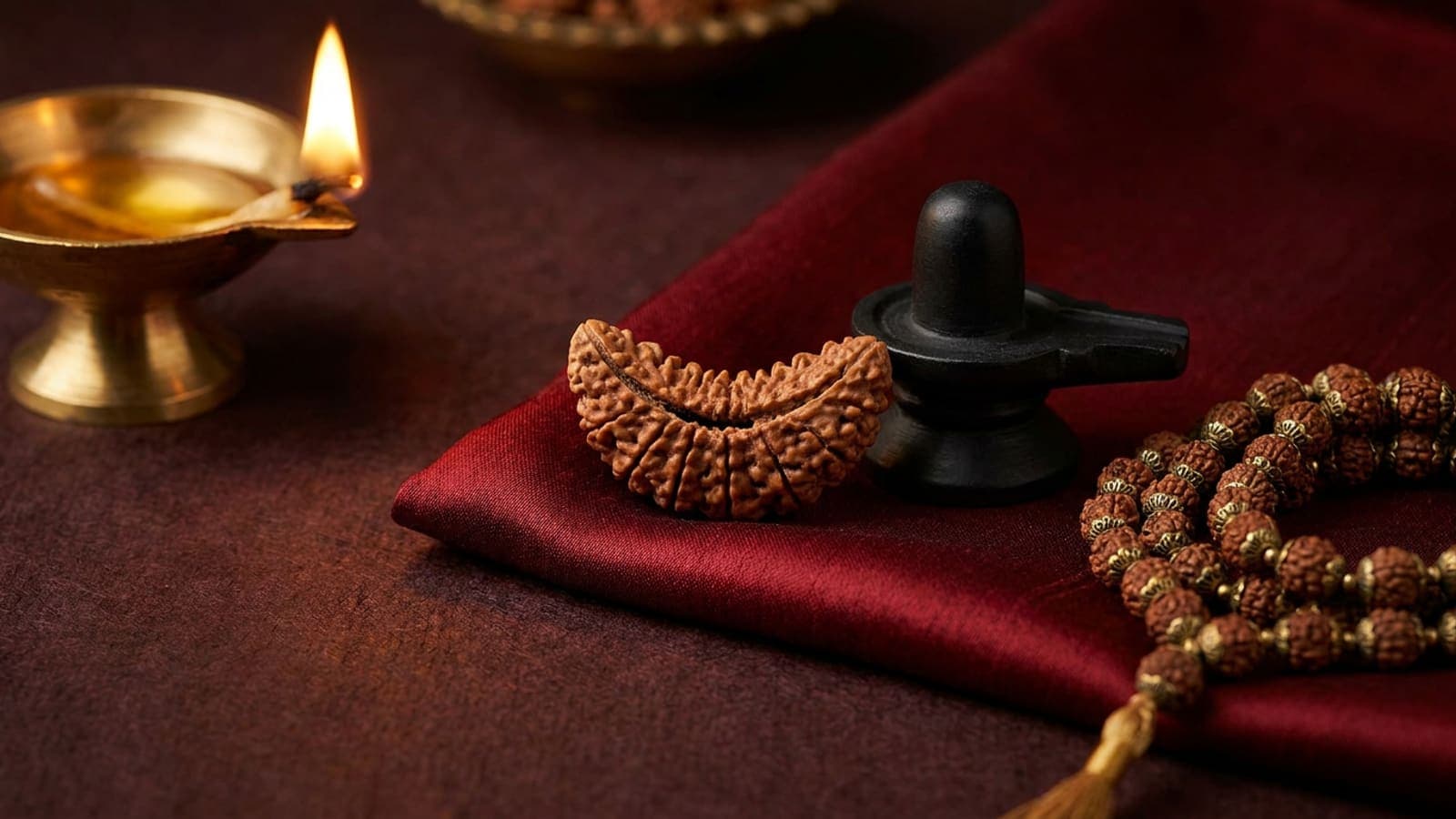 Half-moon 1 mukhi rudraksha bead with single natural face on red silk beside a Shiva lingam and rudraksha mala