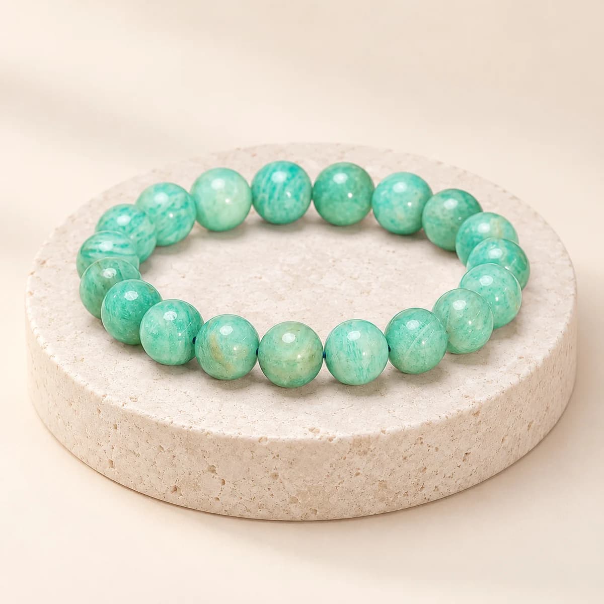 A bead bracelet of polished mint-green amazonite on a light stone pedestal, showing the colour and fine white streaks of the 8 mm beads