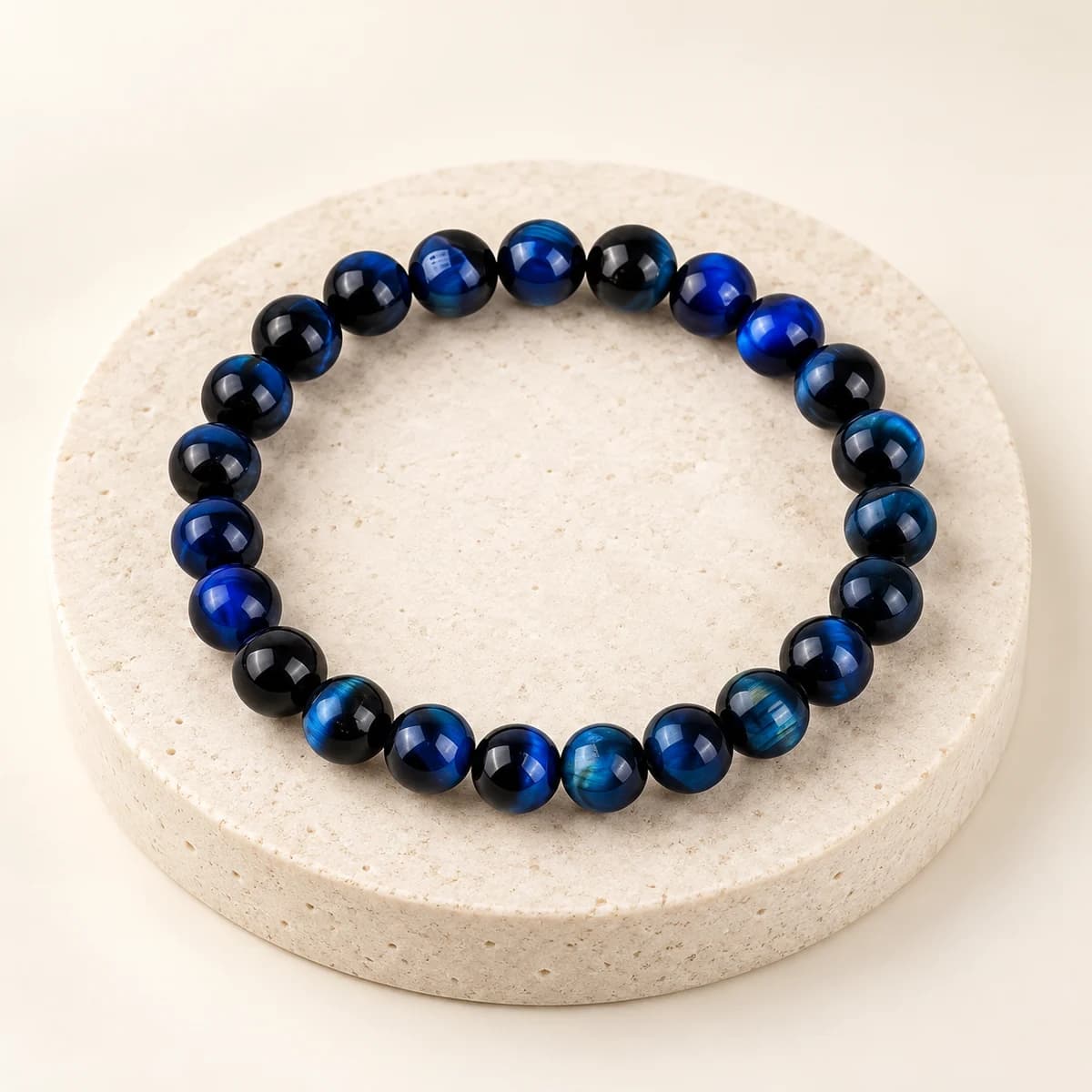 Deep blue 8 mm tiger eye bead bracelet from DivineTatva on a light stone pedestal