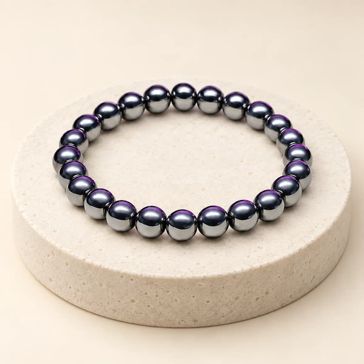 A bead bracelet of polished hematite on a light stone pedestal, showing the metallic grey lustre of the 8 mm beads
