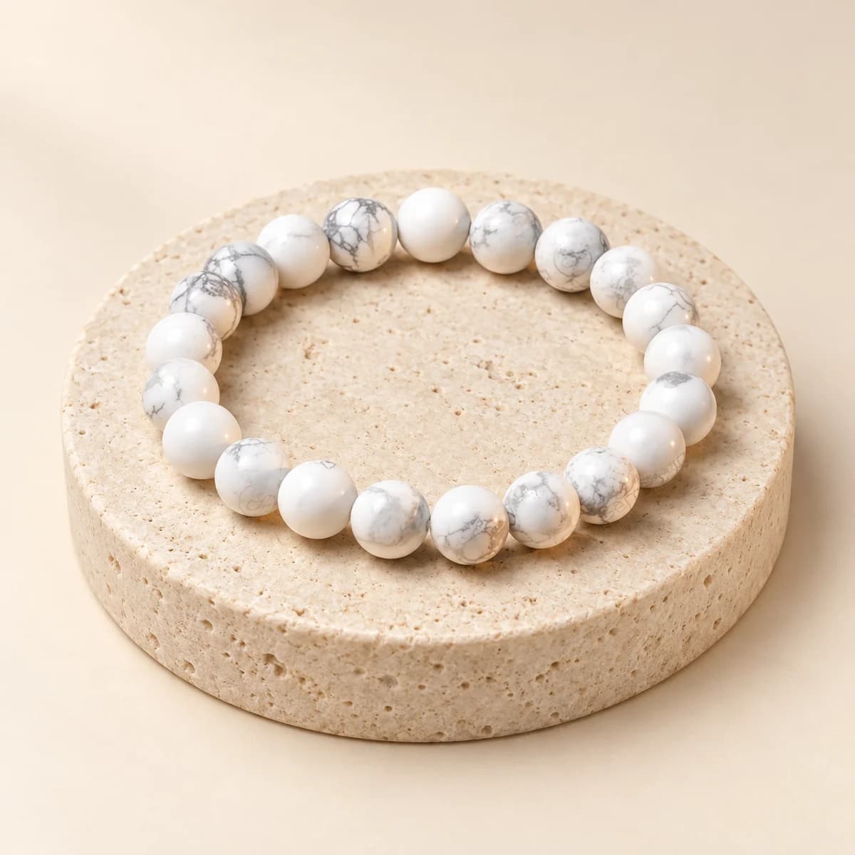 A bead bracelet of polished howlite on a light stone pedestal, showing the white beads with fine grey veining