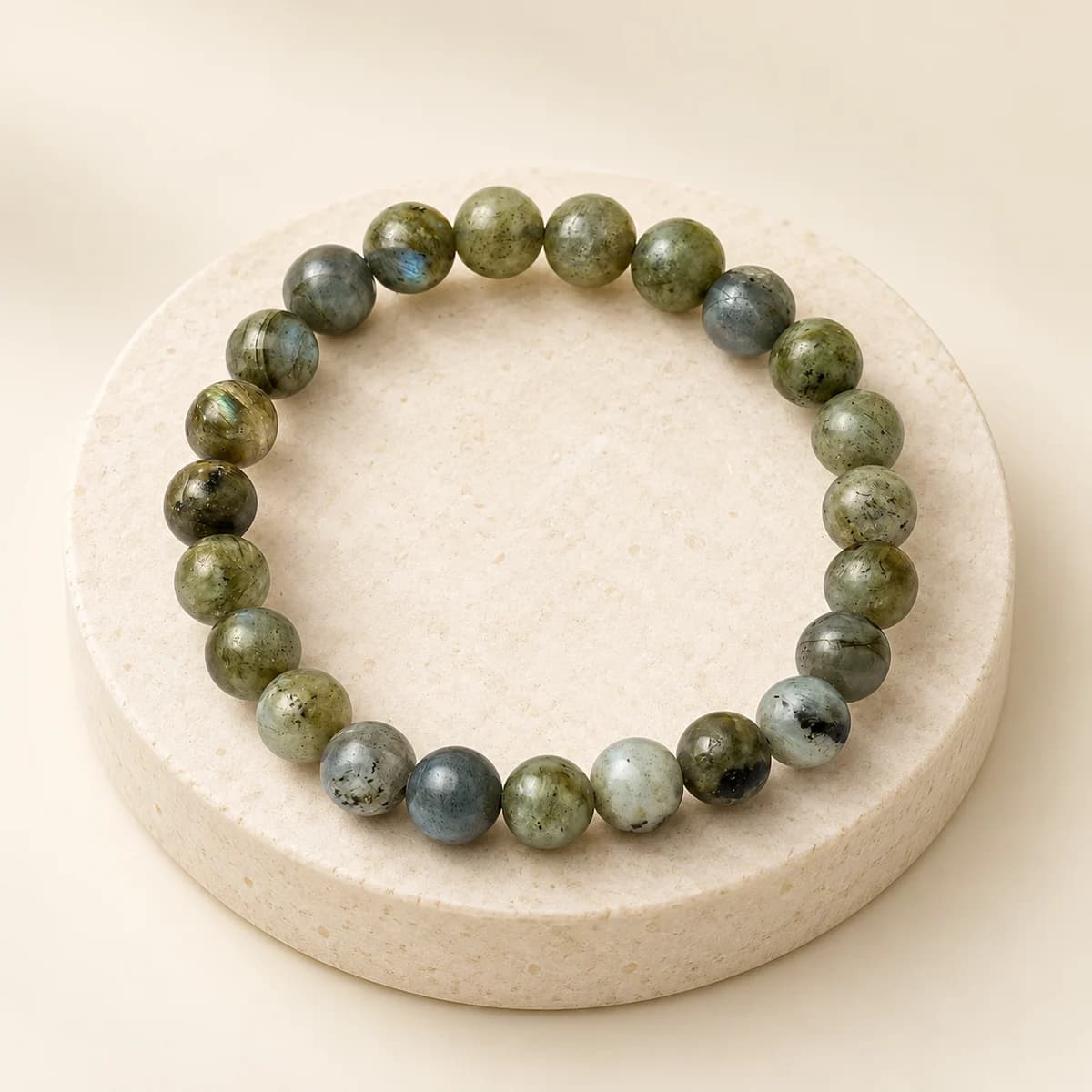 A bead bracelet of polished labradorite, 8 mm beads, on a light stone pedestal