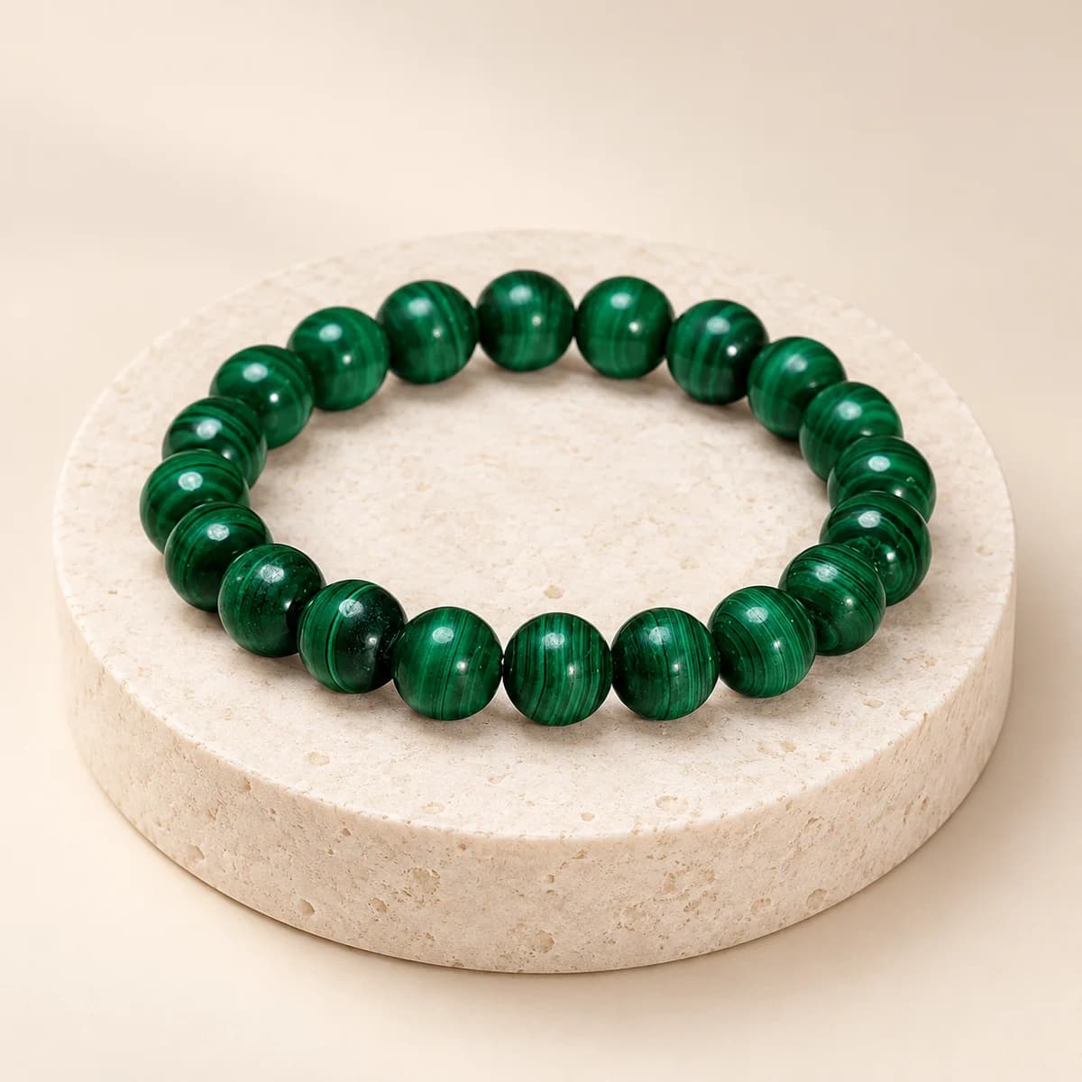 Green 10 mm malachite bead bracelet from DivineTatva on a light stone pedestal