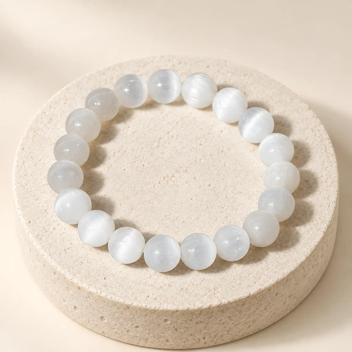 A bead bracelet of polished selenite on a light stone pedestal, showing the soft pearly sheen of the 10 mm beads